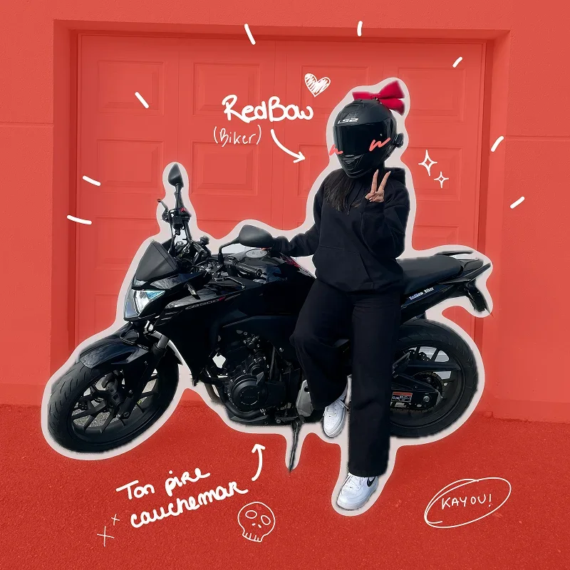 Motarde assise sur une moto noire devant un garage rouge, casque orné d’un nœud rouge