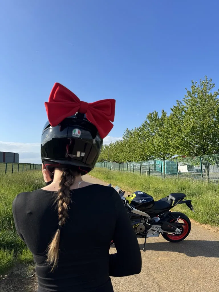 Photo d’Elodie : grand nœud rouge porté sur un casque noir près d’une moto